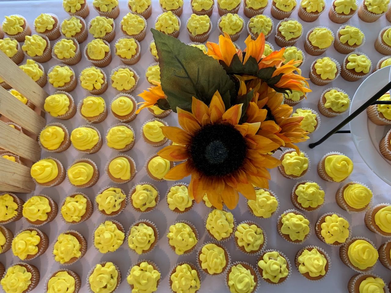 vase of sunflowers placed amid rows of cupcakes with yellow icing on a party table