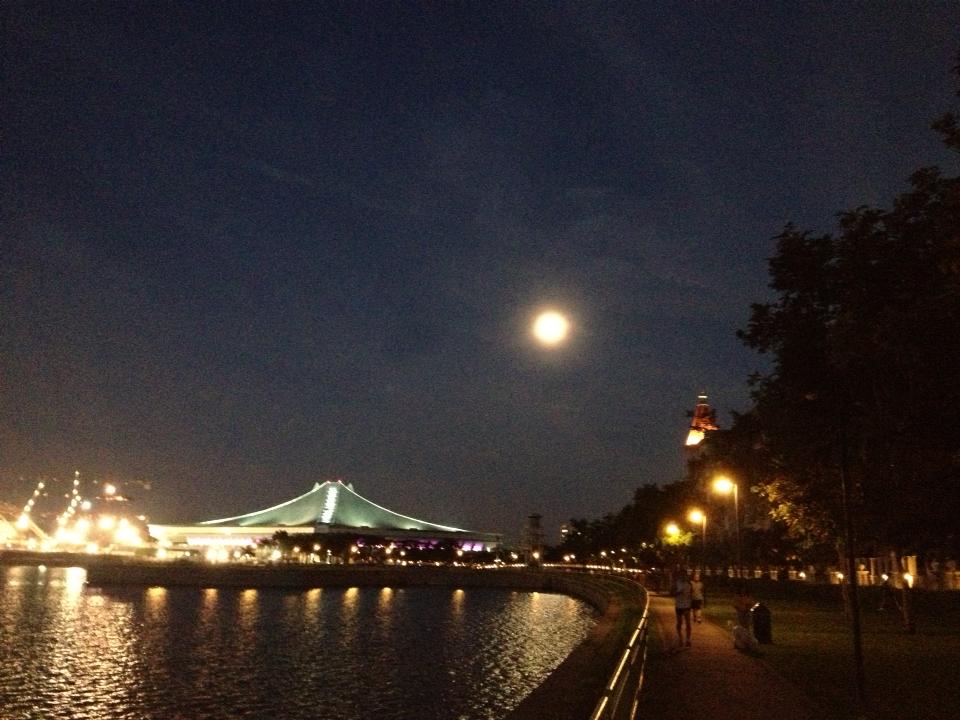 full moon in the night sky over a river and a riverside walkway in a city