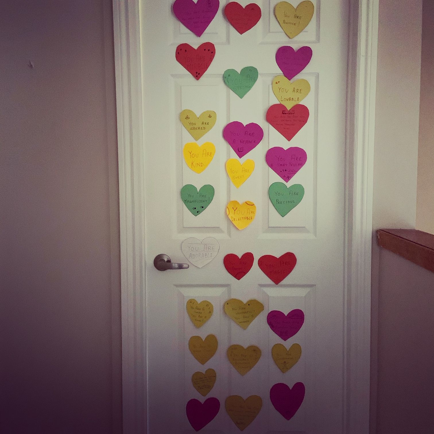 a closed door with twenty-nine paper hearts taped to it