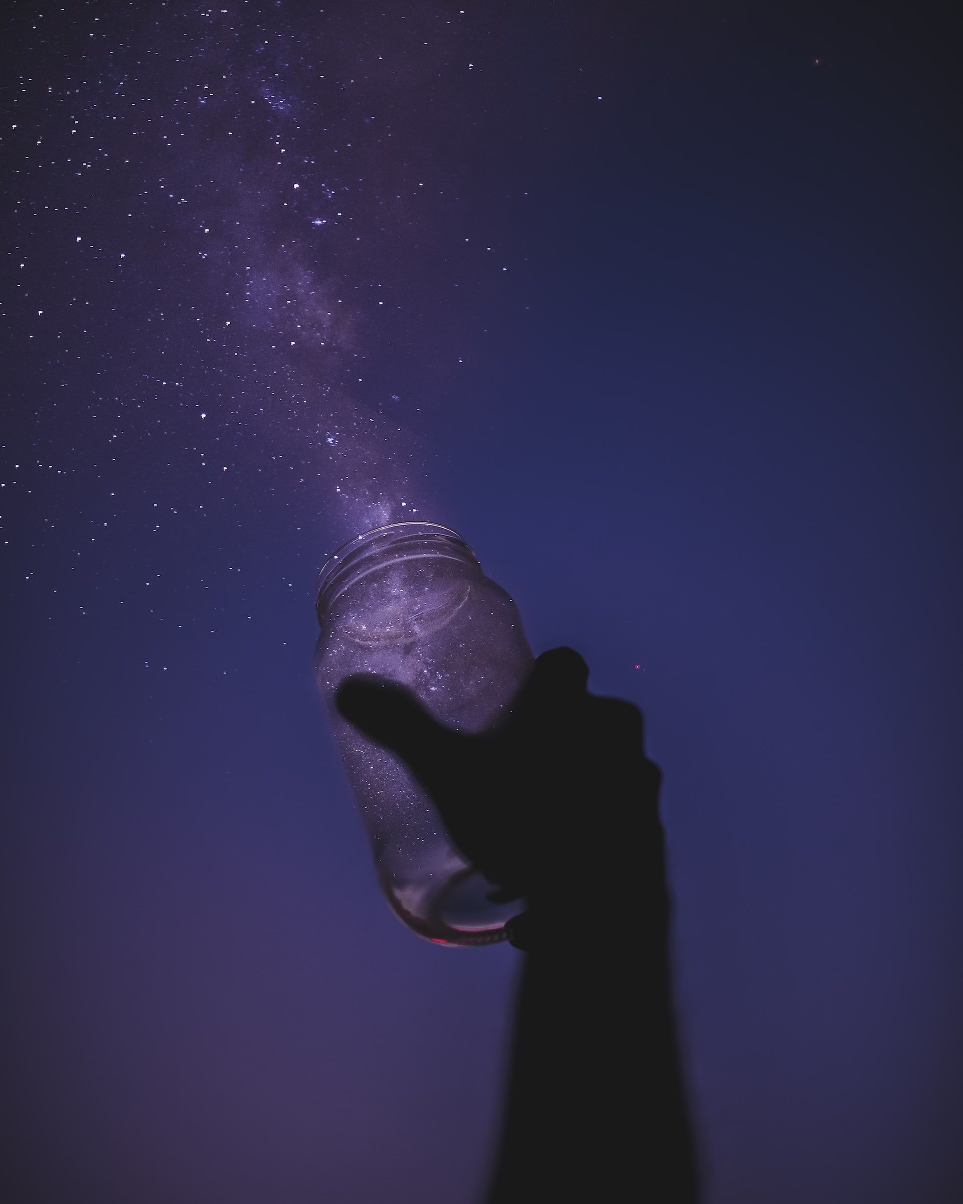 a hand holding a jar that catches twinkling points of light from a dusky sky