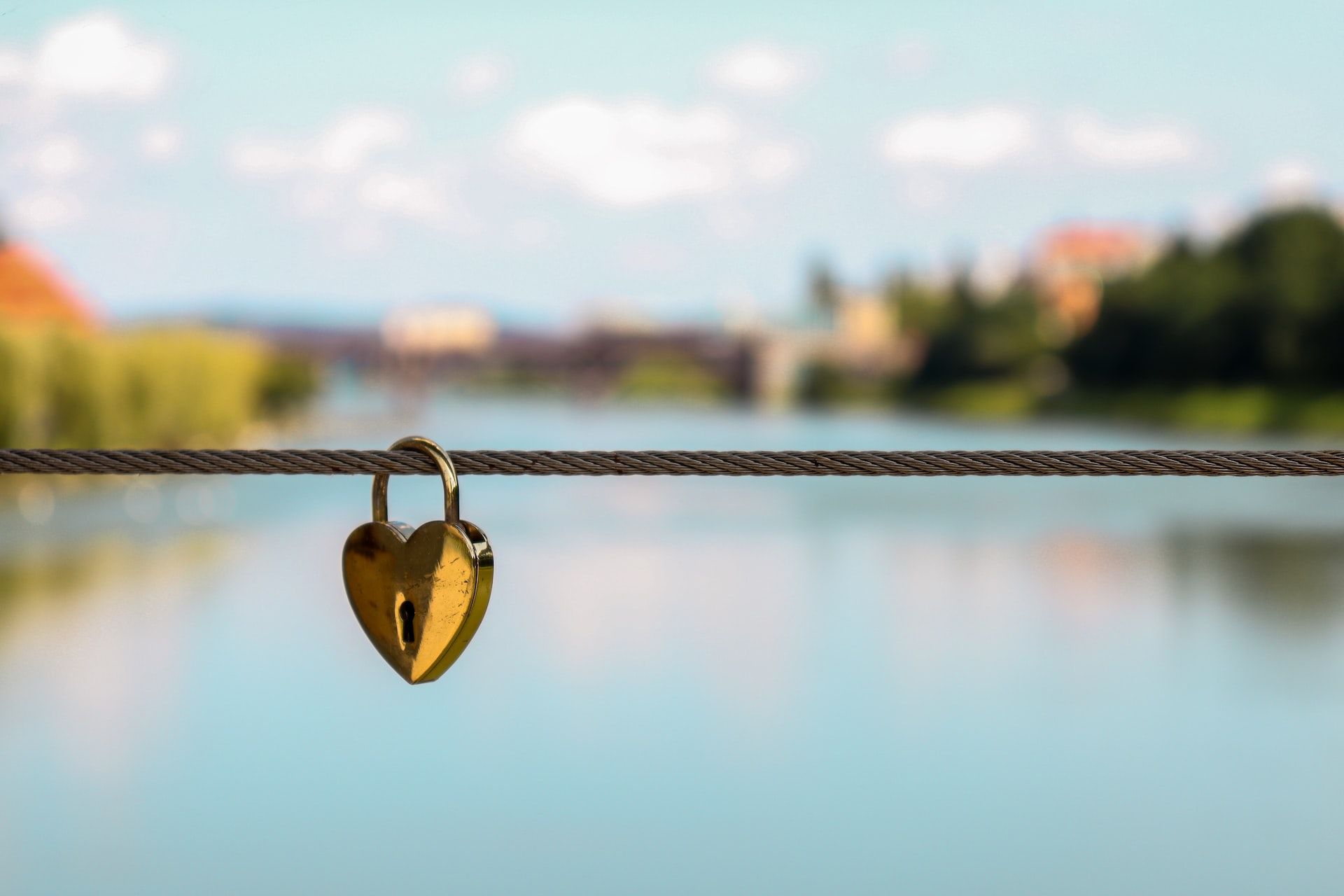 heart-shaped lock on a string against a blurred background of a river and blue skies