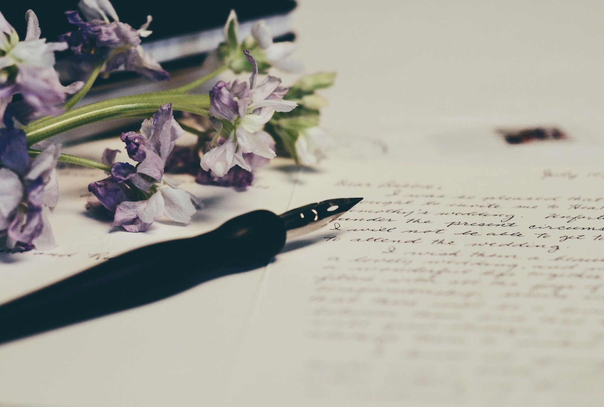 Fountain pen on a sheet of paper with handwriting on it and a bunch of lavender flowers