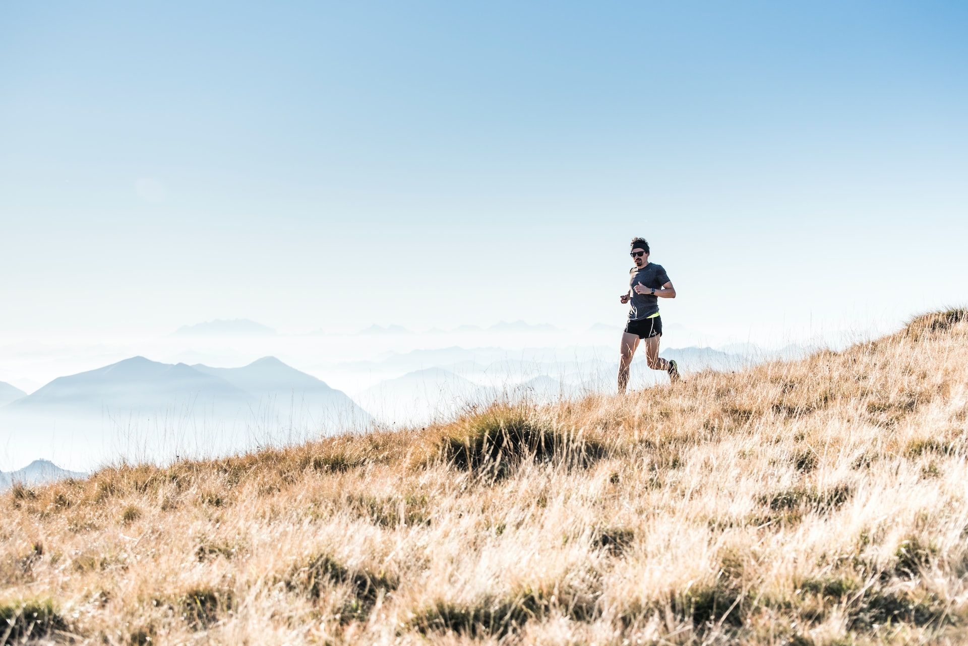 man running downhill on a brown grassy slope with distant hills in the background