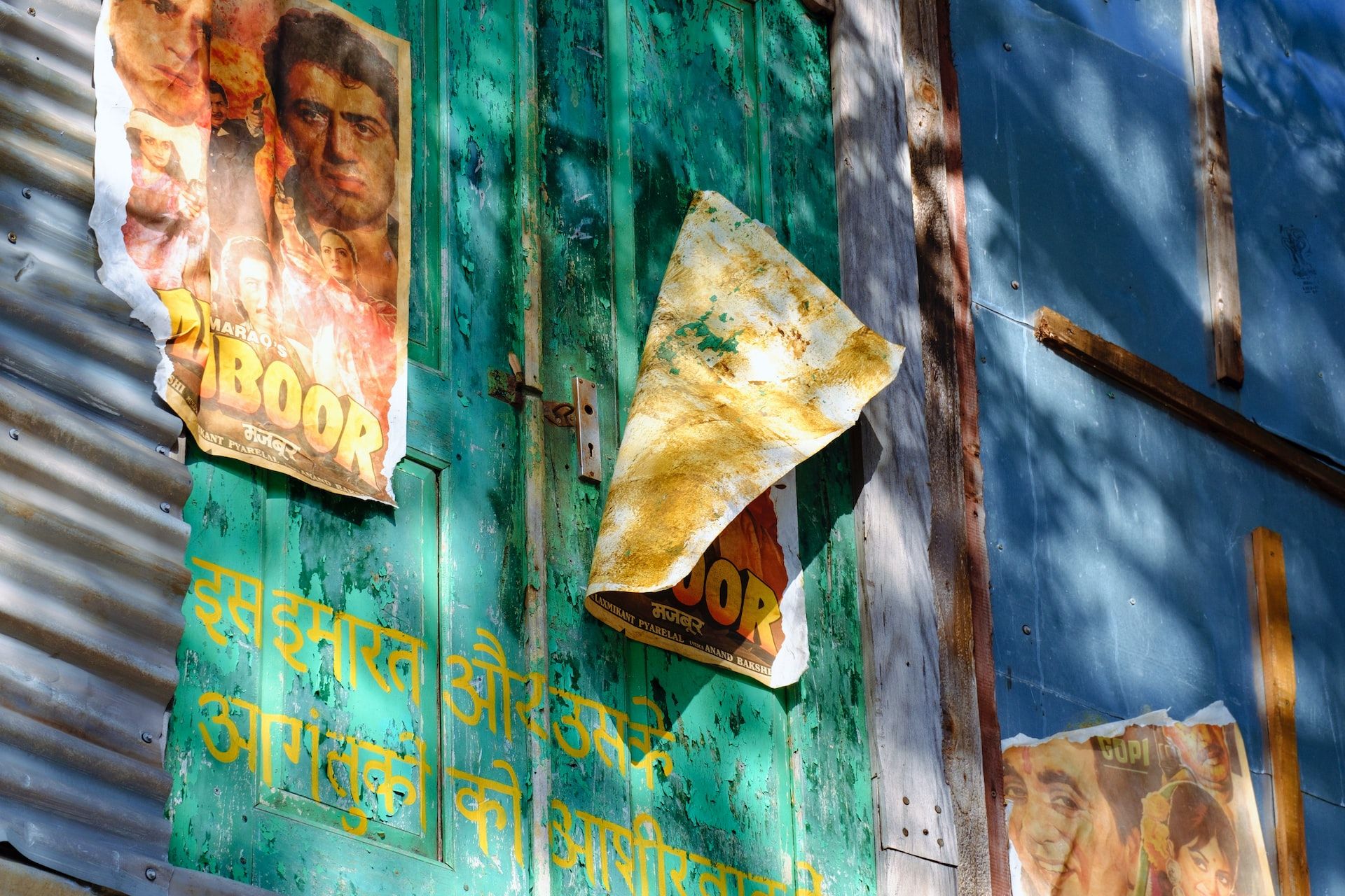 weathered Bollywood movie posters pasted to a blue and green wall