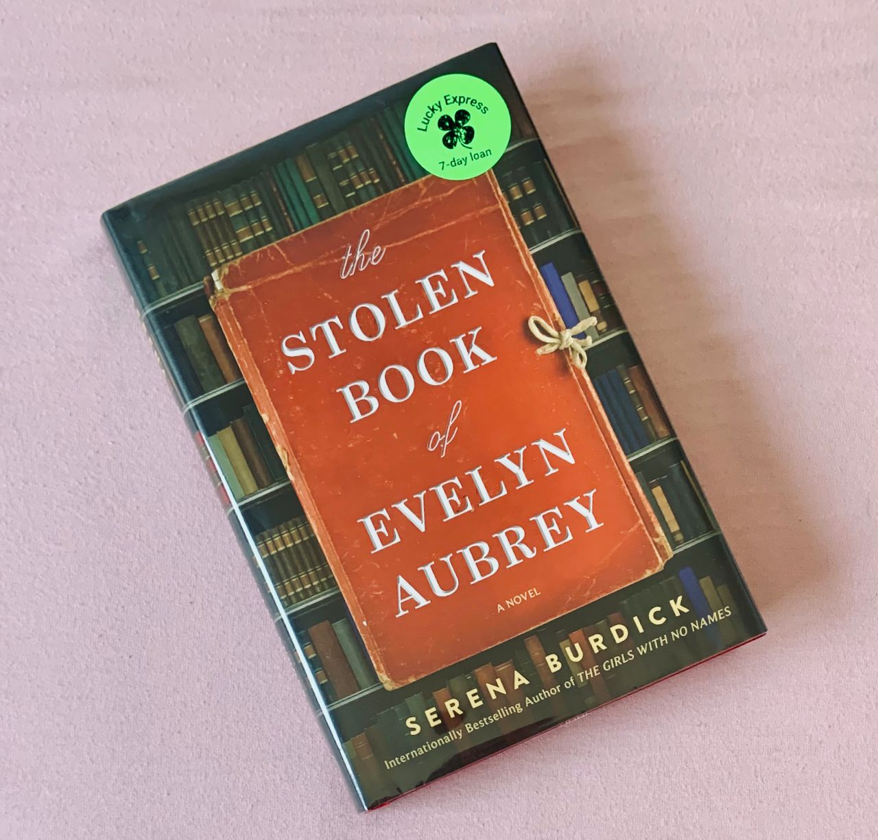 Hardcover copy of The Stolen Book of Evelyn Aubrey by Serena Burdick featuring a red journal against a bookshelf