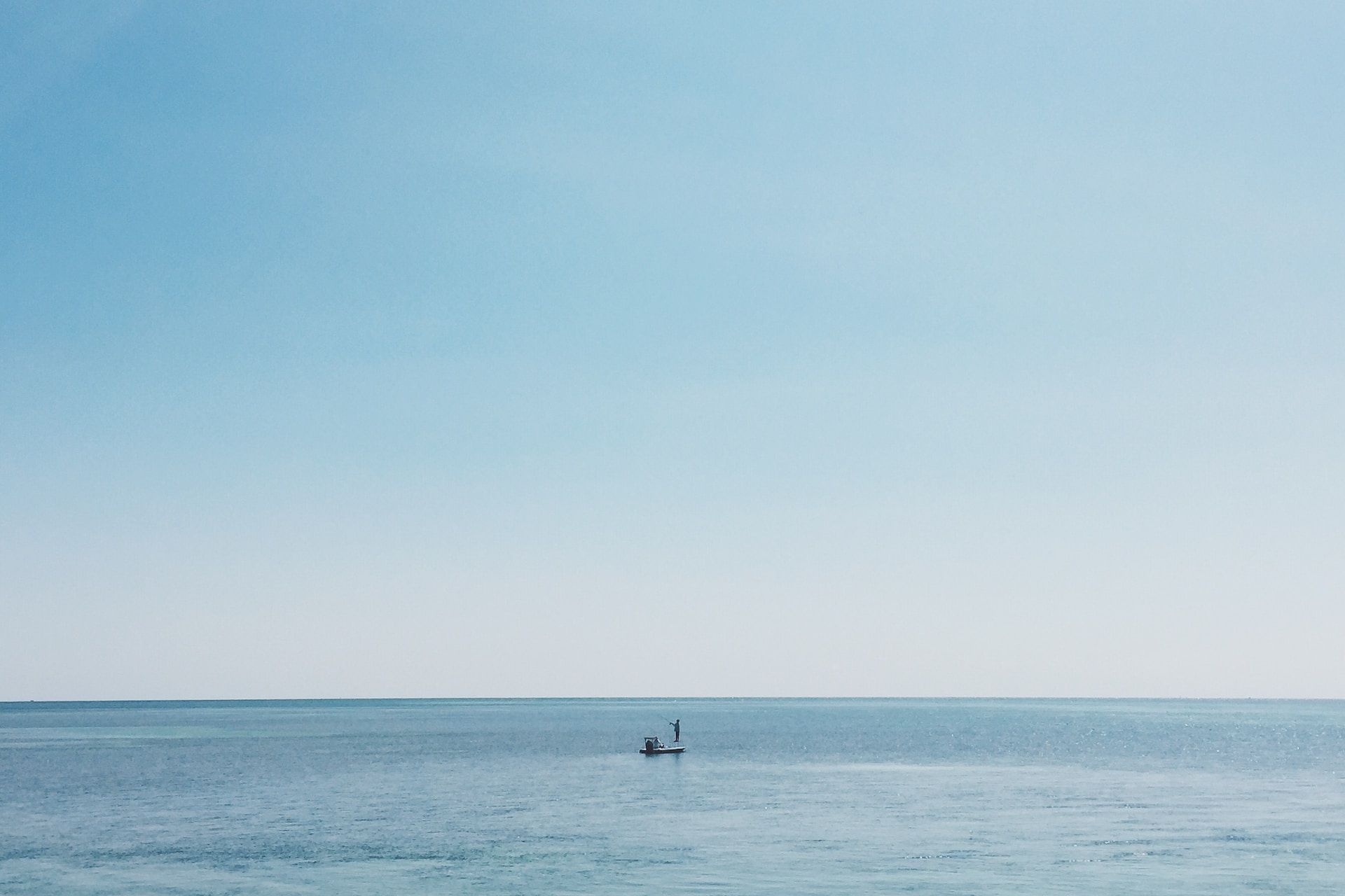 fisherman in a distant small boat on a blue ocean under a blue sky