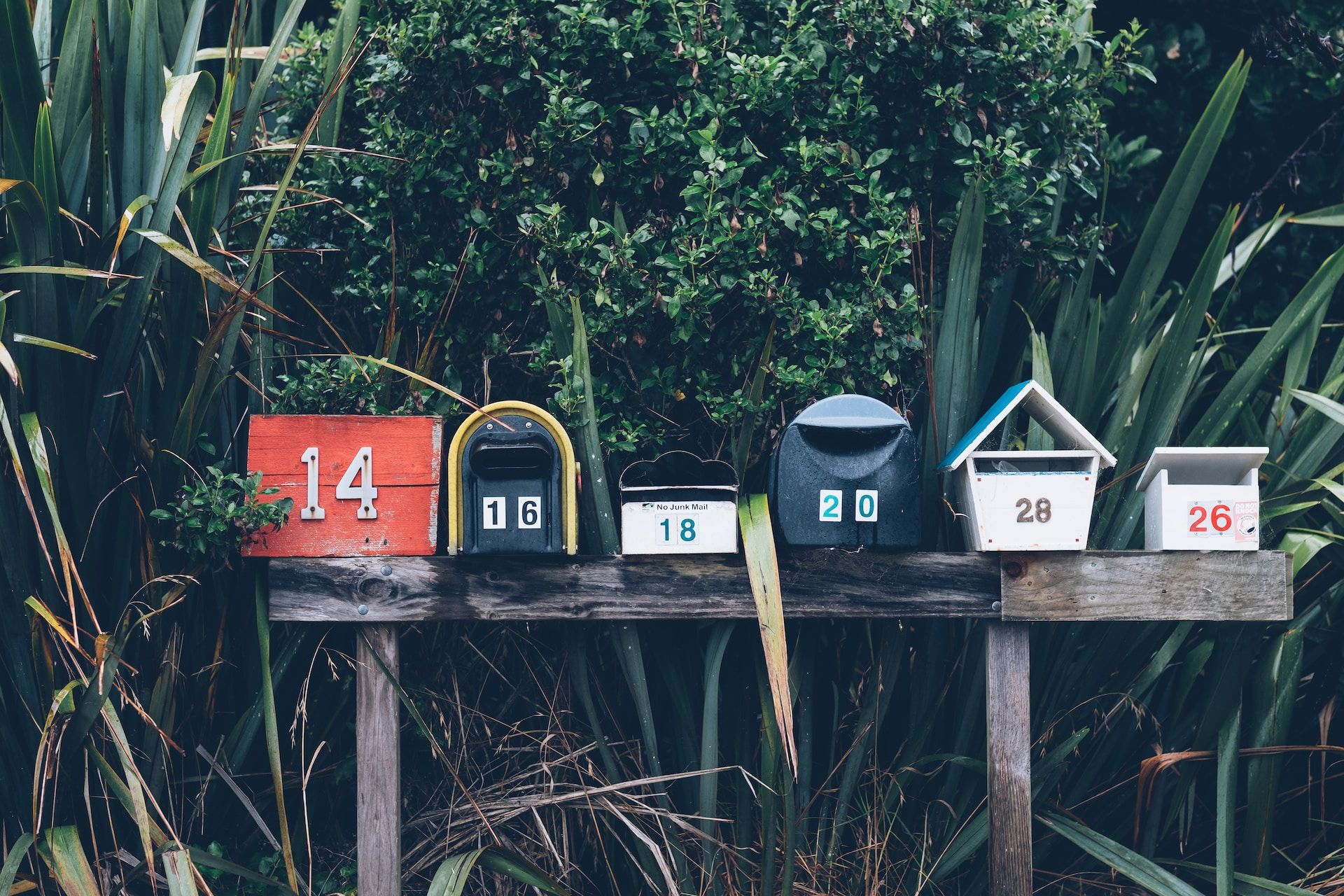 Six numbered mailboxes of different colours set atop a wooden stand