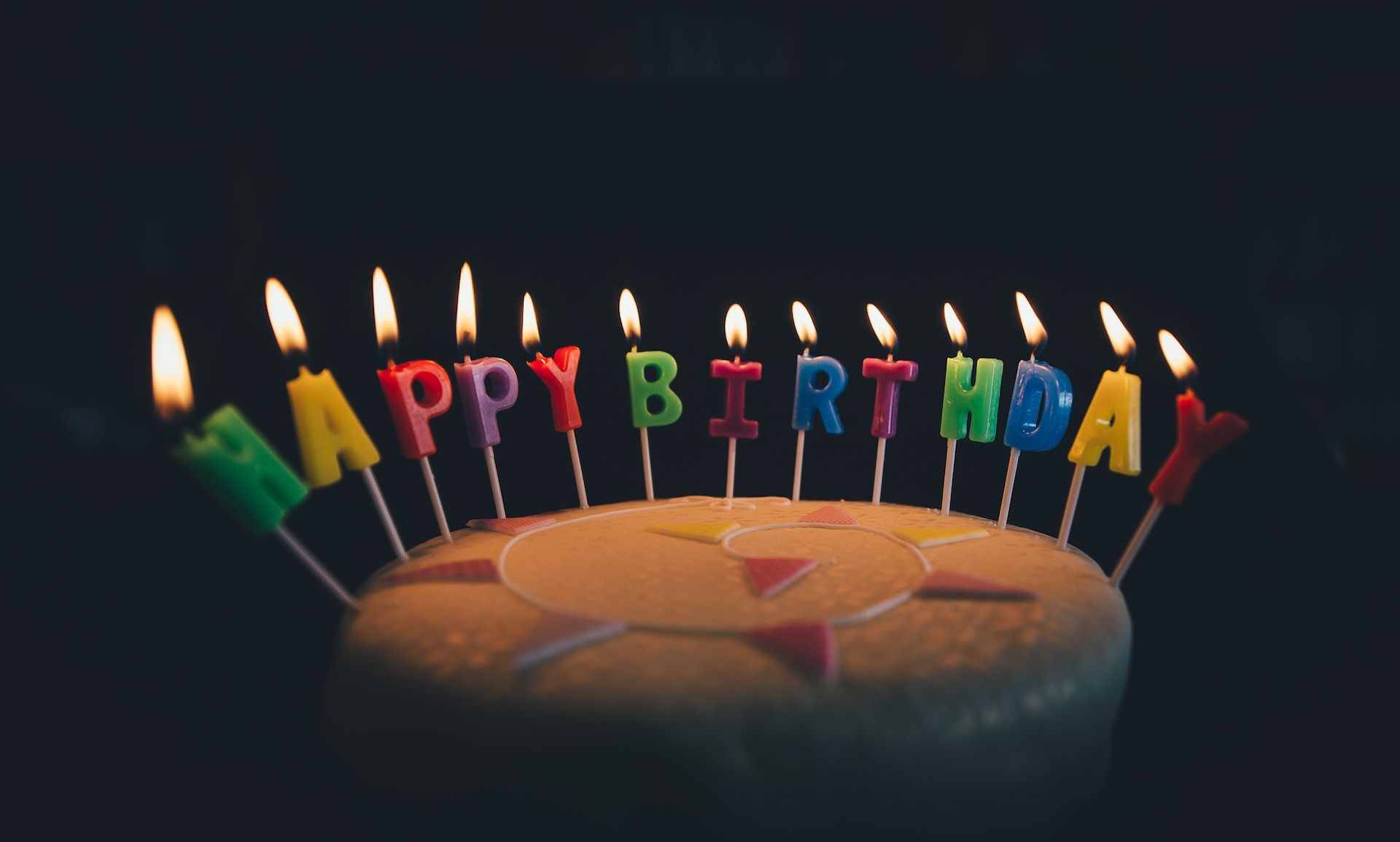 birthday cake with lit candles in the shape of the letters of happy birthday