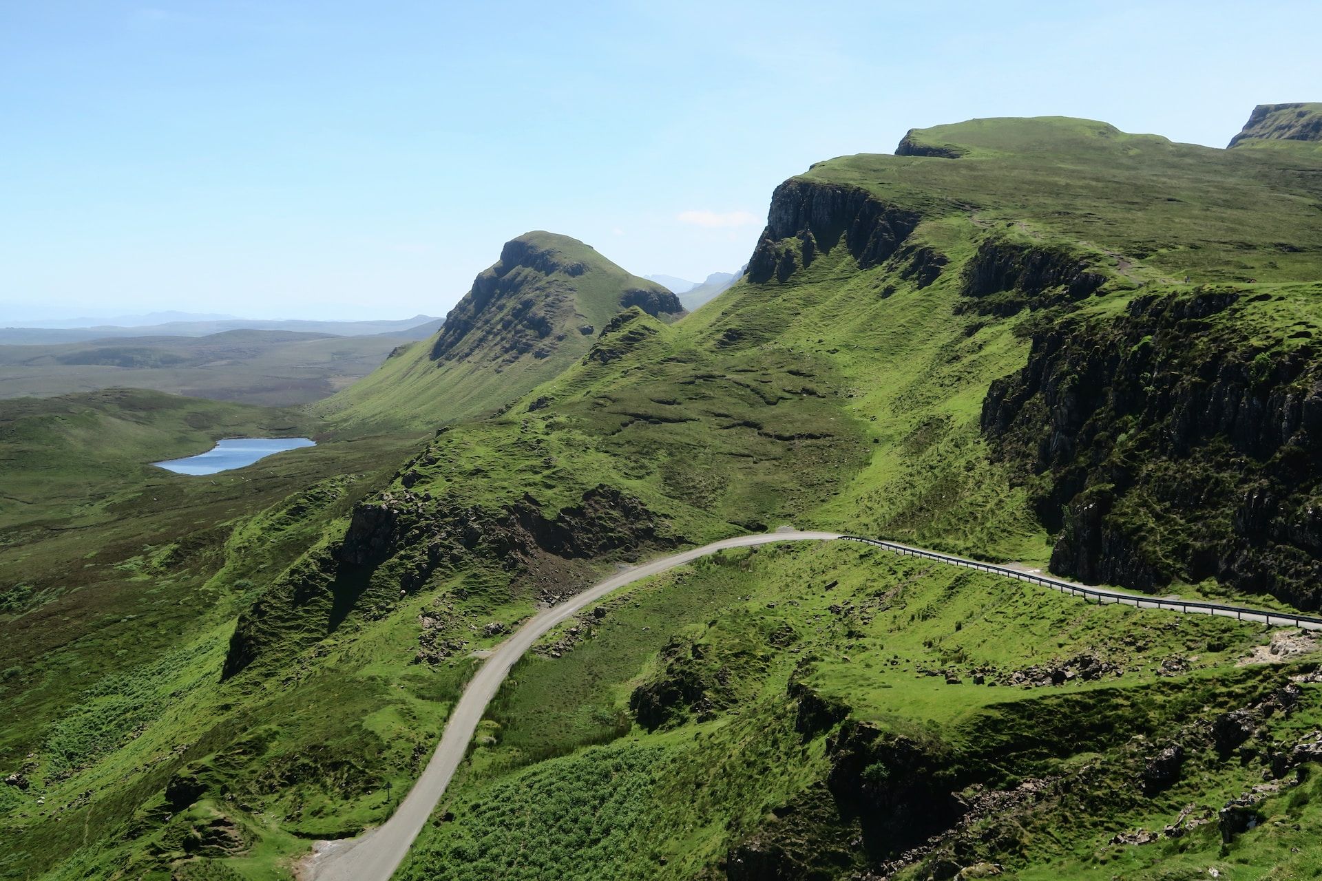 concrete road winding through a green mountain under a blue sky