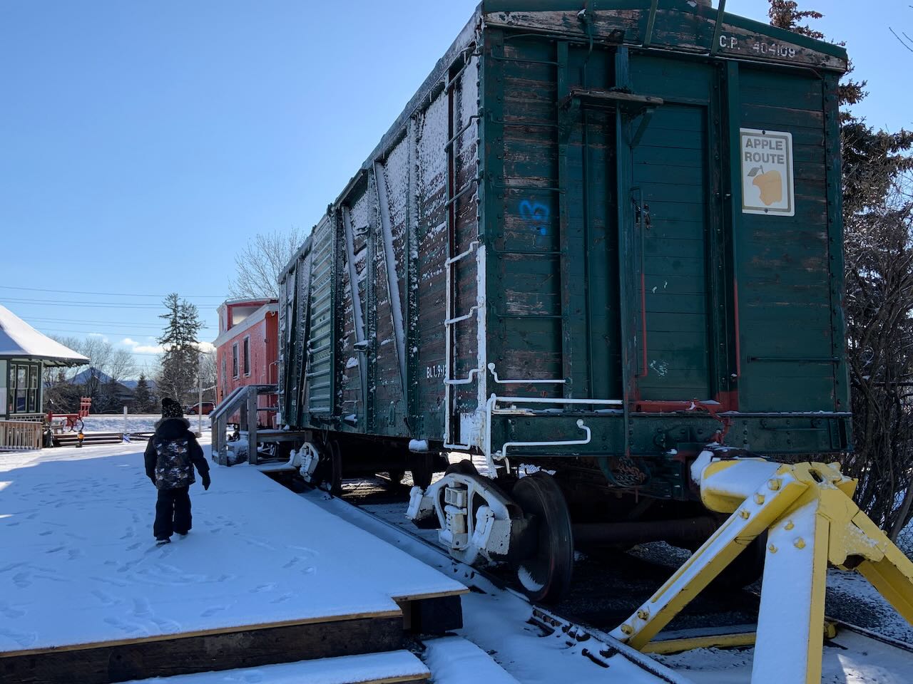 a red caboose coupled to a green freight car with a poster on it saying 'apple route'