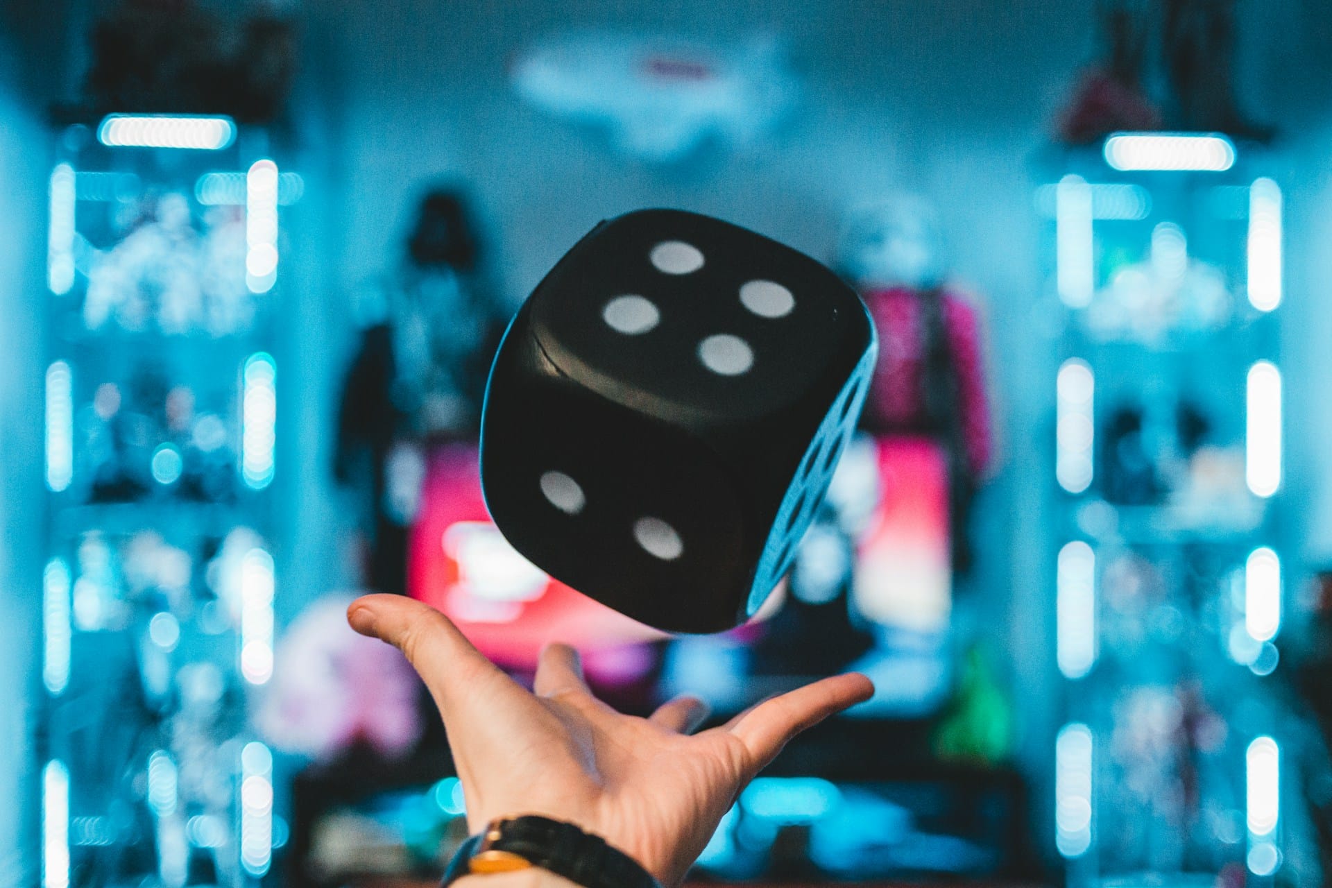 image of a hand throwing a large black dice into the air against a blurred background of neon lights