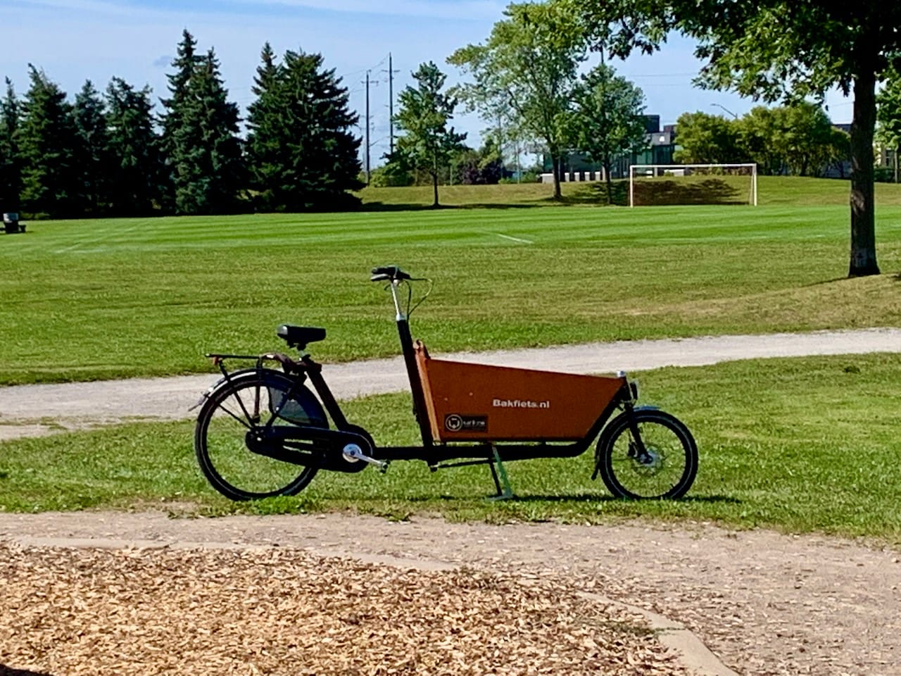 a bakfiets (Dutch cargo bike) parked in front of a soccer field