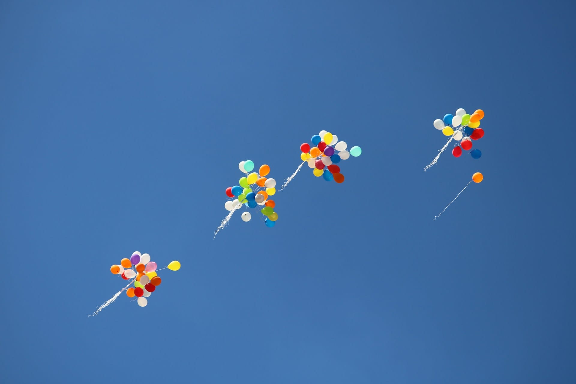 clusters of balloons flying away in a blue sky
