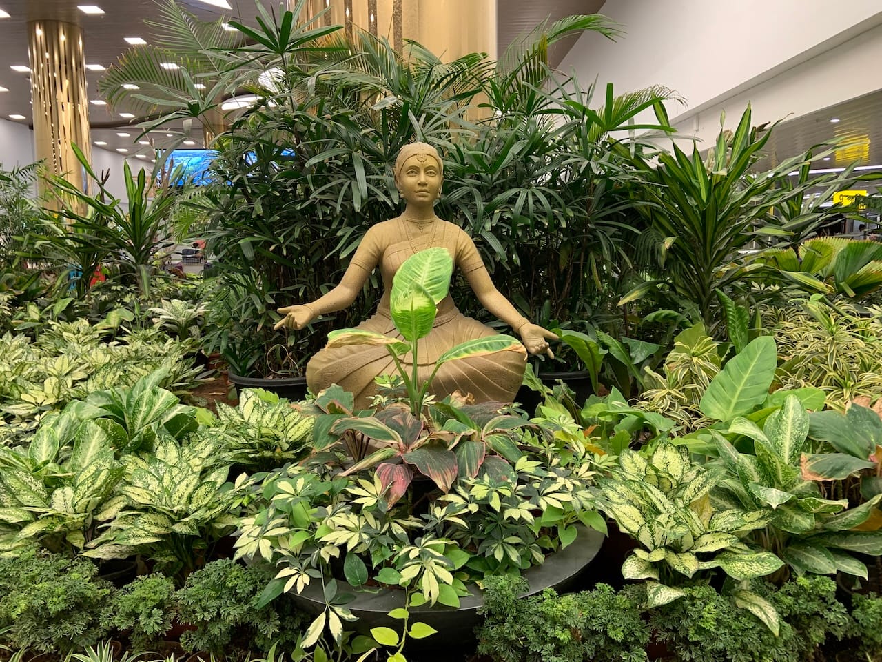 a bronze idol of a dancer surrounded by plants at the Chennai International Airport