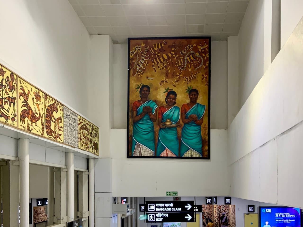 a large painting of three women welcoming visitors with a plate of aarti