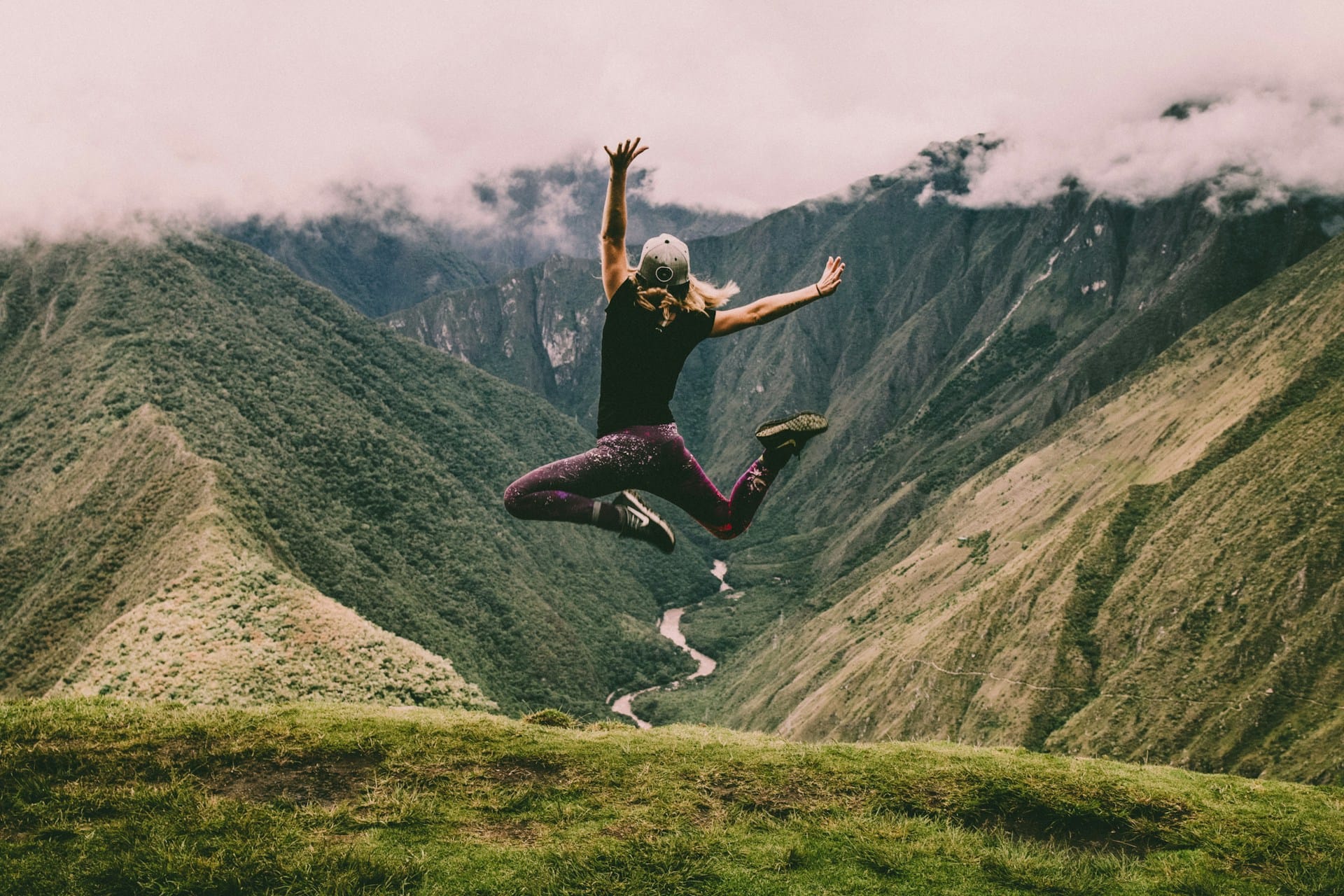 person jumping atop a mountain against the backdrop of mountains and a valley