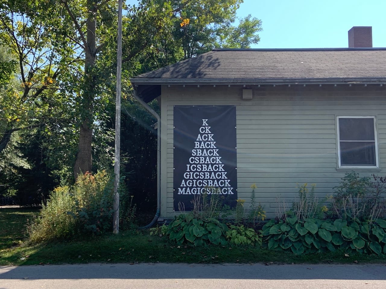 a one-storeyed house with a large black poster taped to its wall reading 'MAGICSBACK' adding one letter at a time
