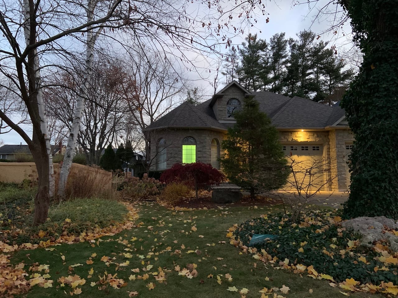 a suburban house with a lone bay window lit with green light from within and overlooking a front lawn