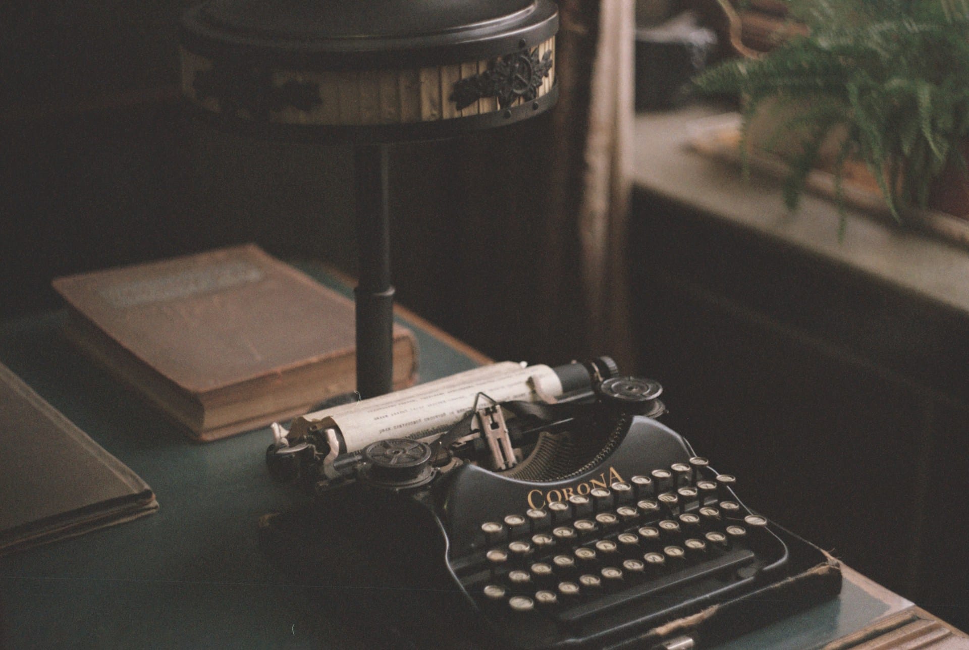 a Corona typewriter on a table with a book behind it