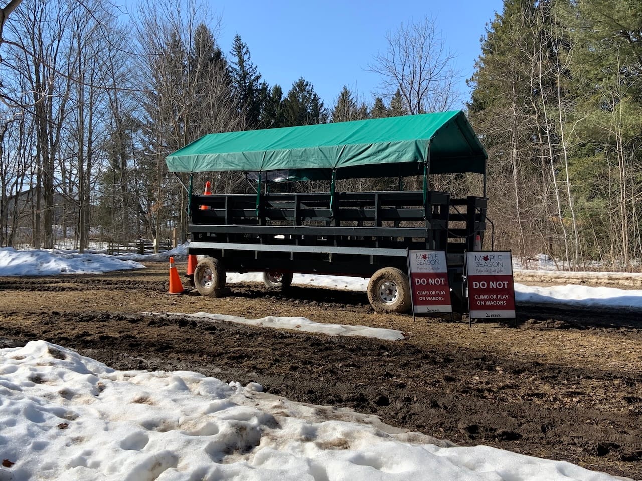 a wagon positioned on a muddy field surrounded by orange cones and boards stating 'Do not climb or play on wagon'.
