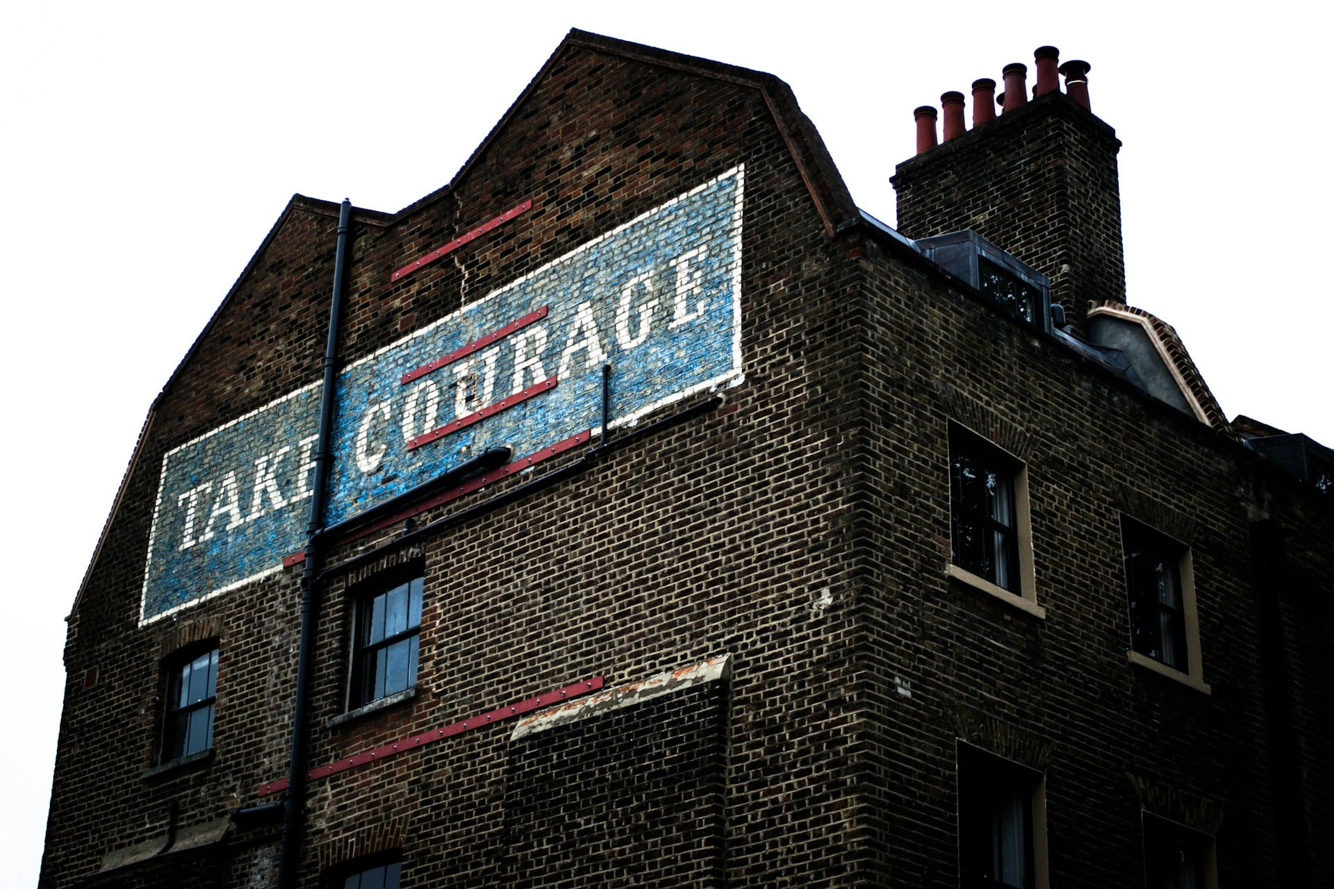 an old brick home with the words 'TAKE COURAGE' painted above the topmost windows