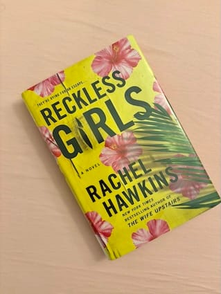 Hardcover format of Reckless Girls by Rachel Hawkins featuring pink tropical flowers and a palm frond against a bright yellow background