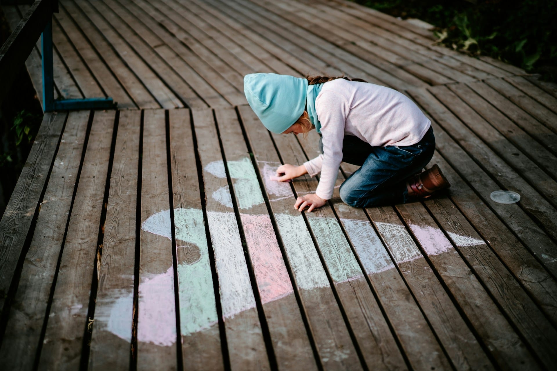 a little child hunched over a wooden deck and drawing heart shapes with chalk