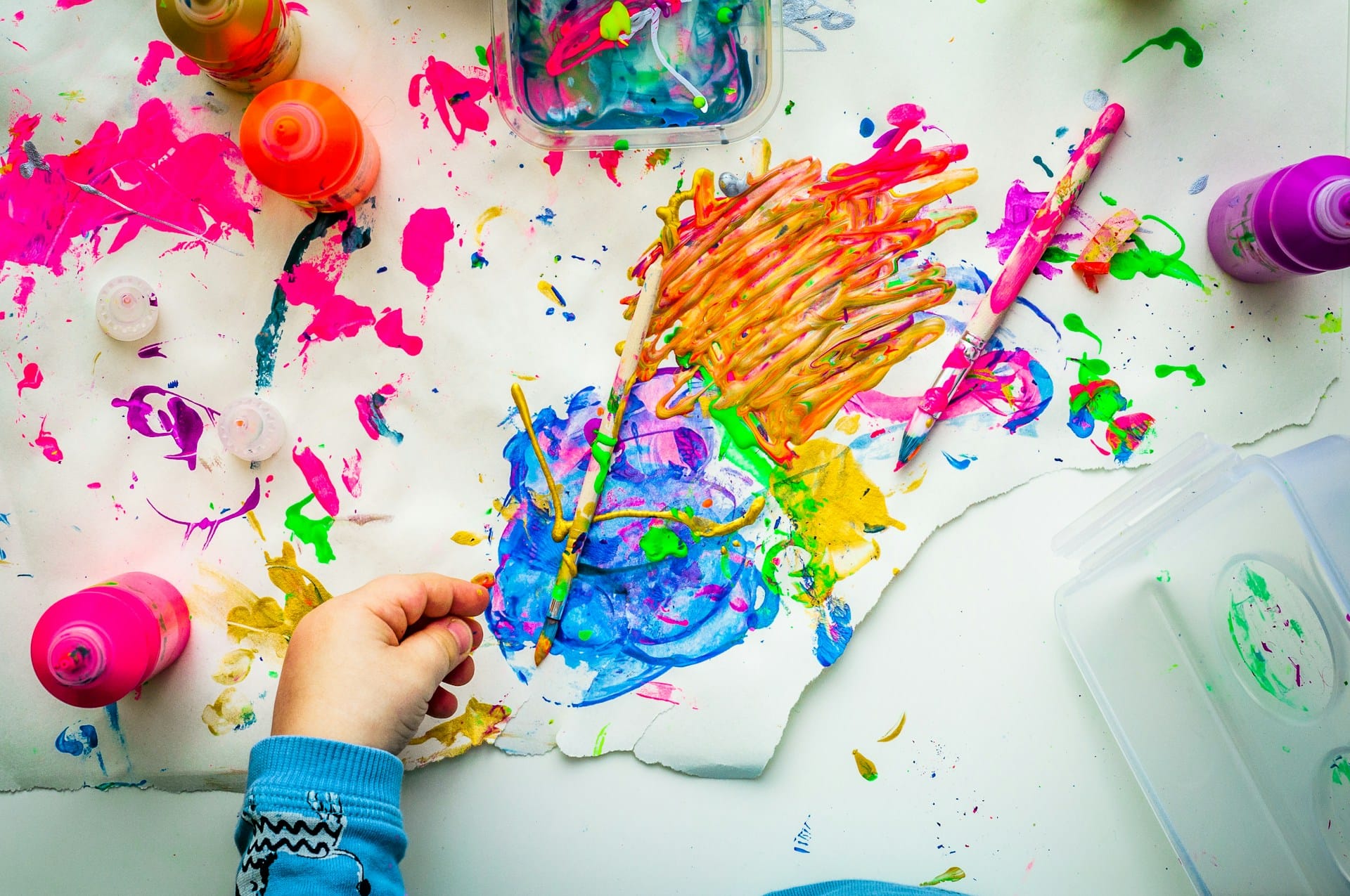 a child's hand spreading random colours on a white sheet of paper