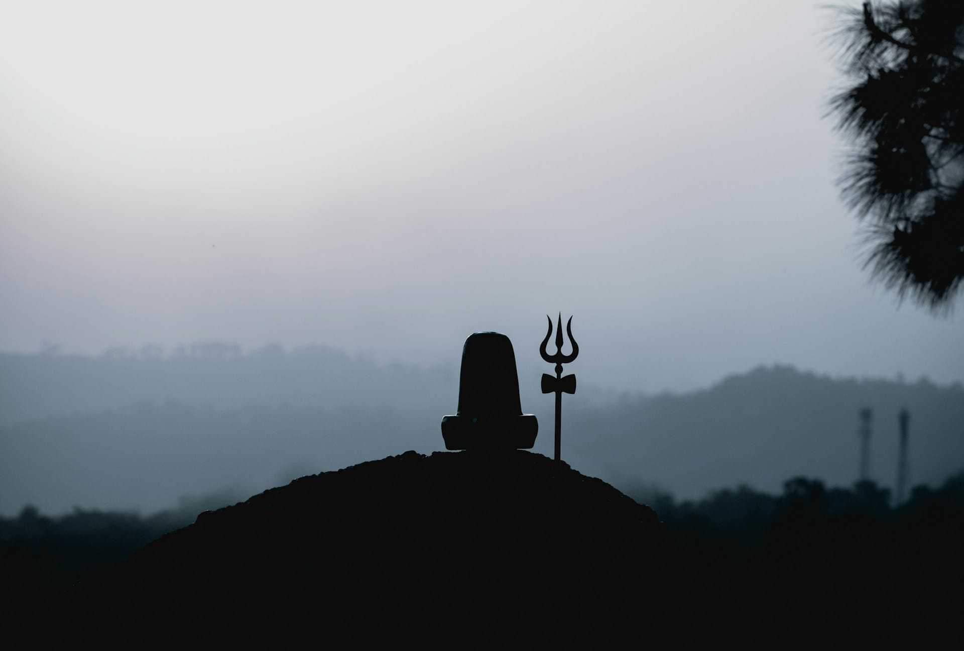 silhouette of a Shivling and a trishul (trident) against a backdrop of distant mountains