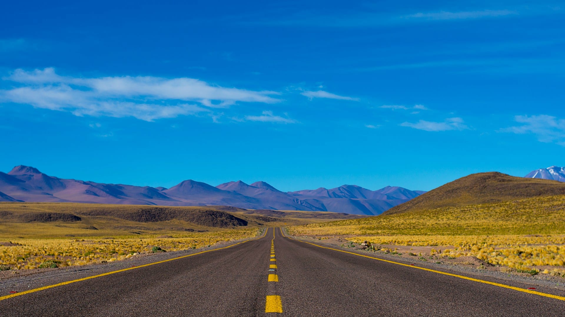 paved road unfurling towards distant mountains under a blue sky