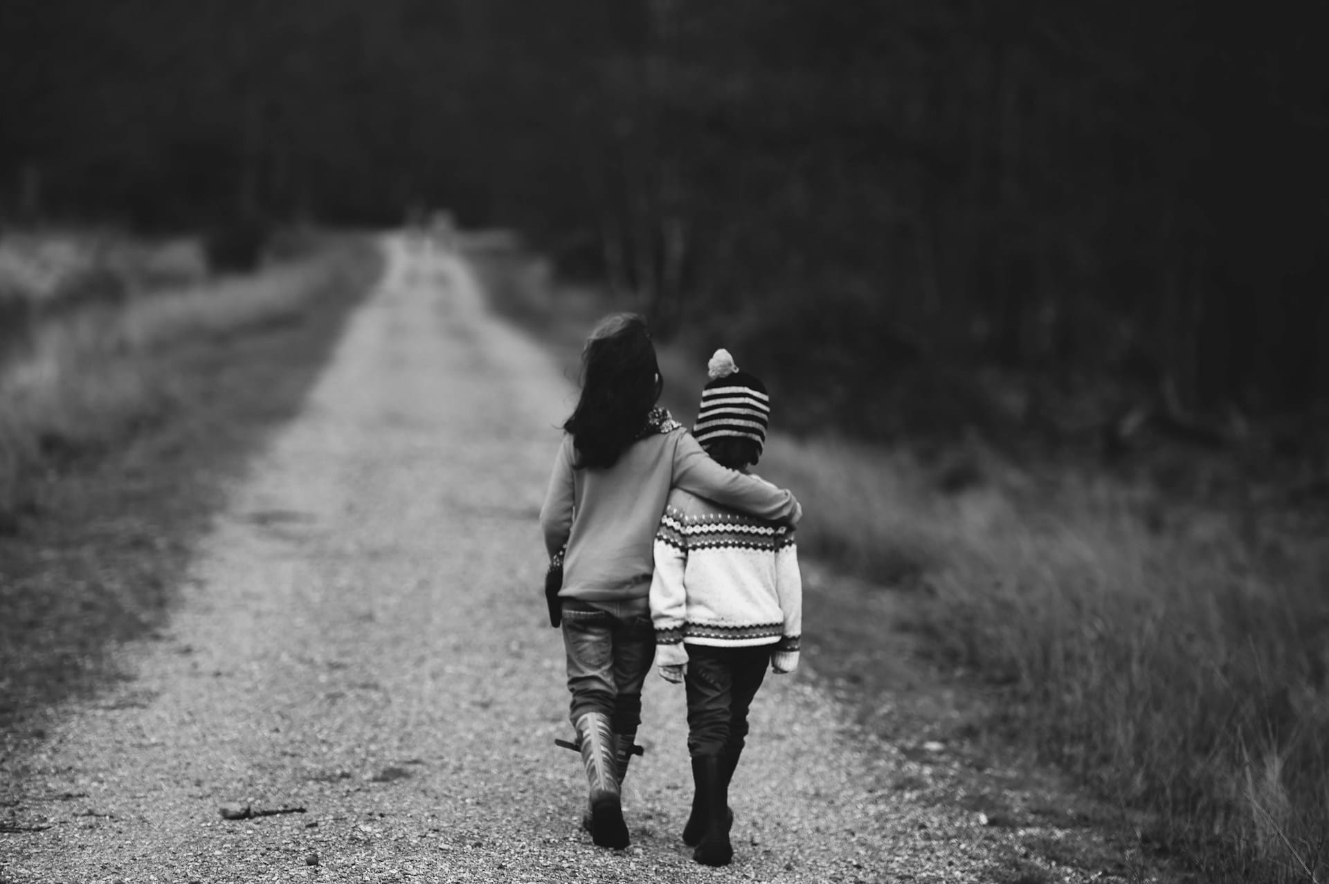 rear black-and-white image of two children walking on a dirt lane through the woods
