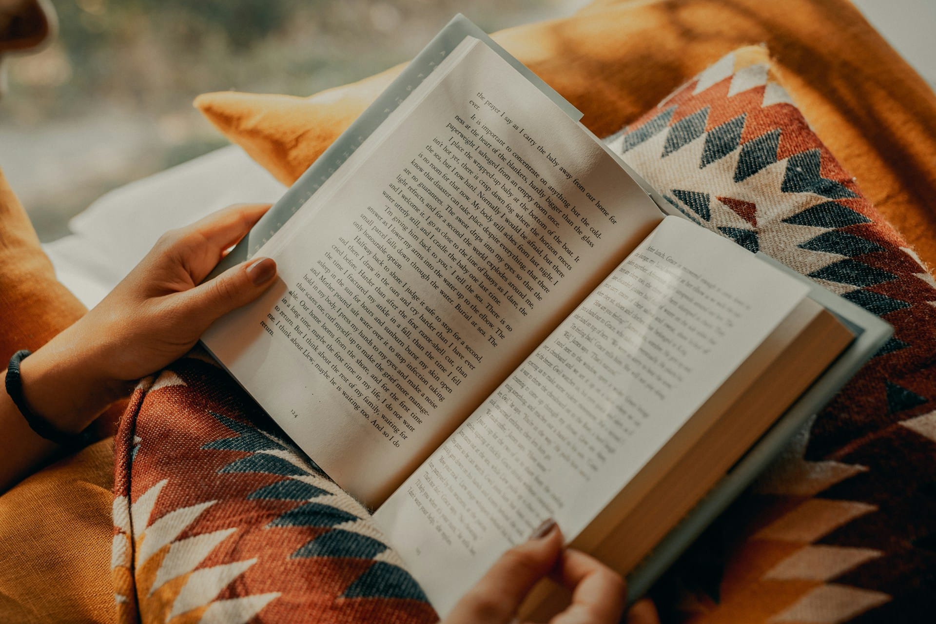 open book held by an unseen person against autumn-themed pillows