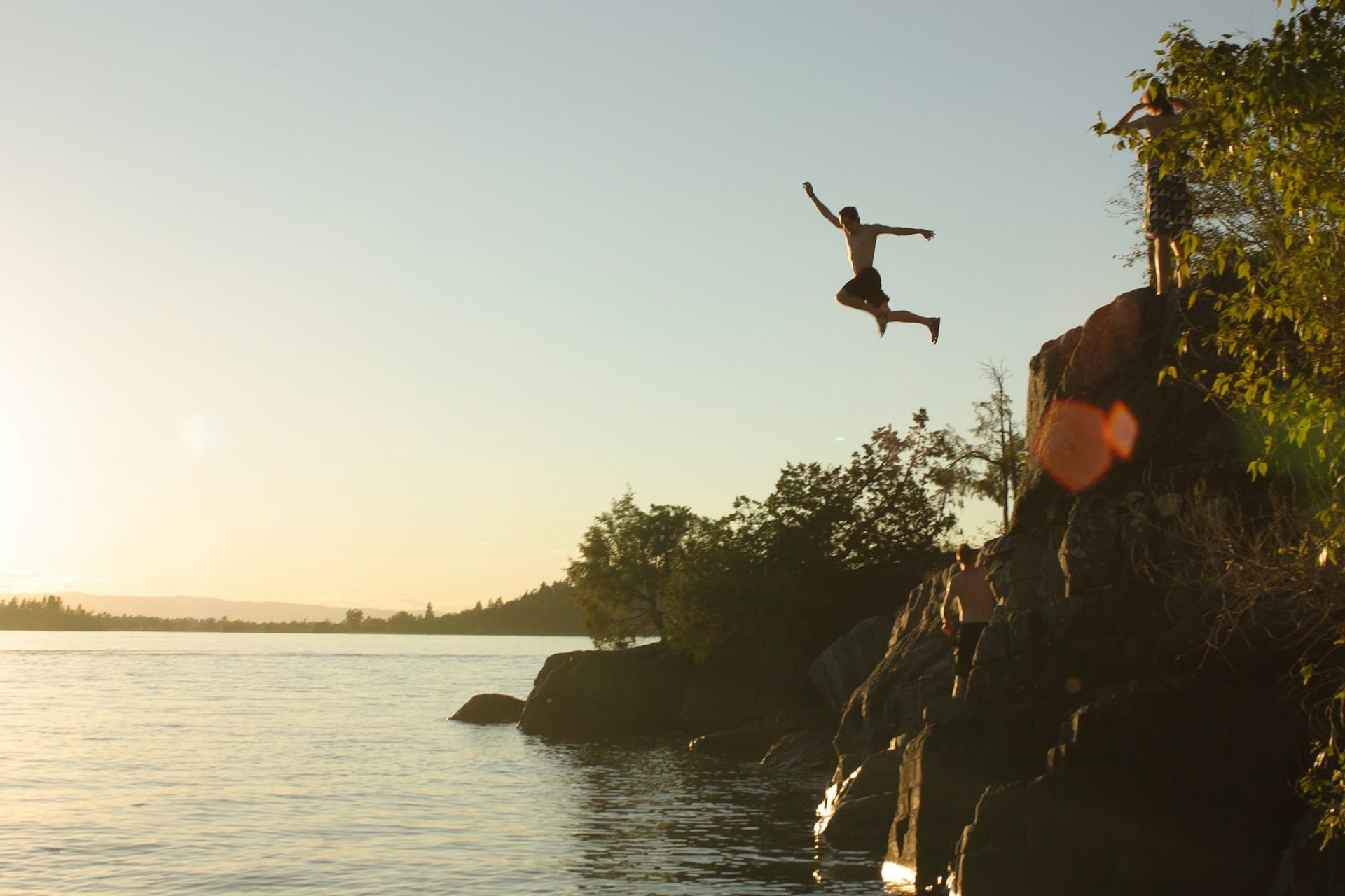 man diving from a clifftop into a water body at sunset