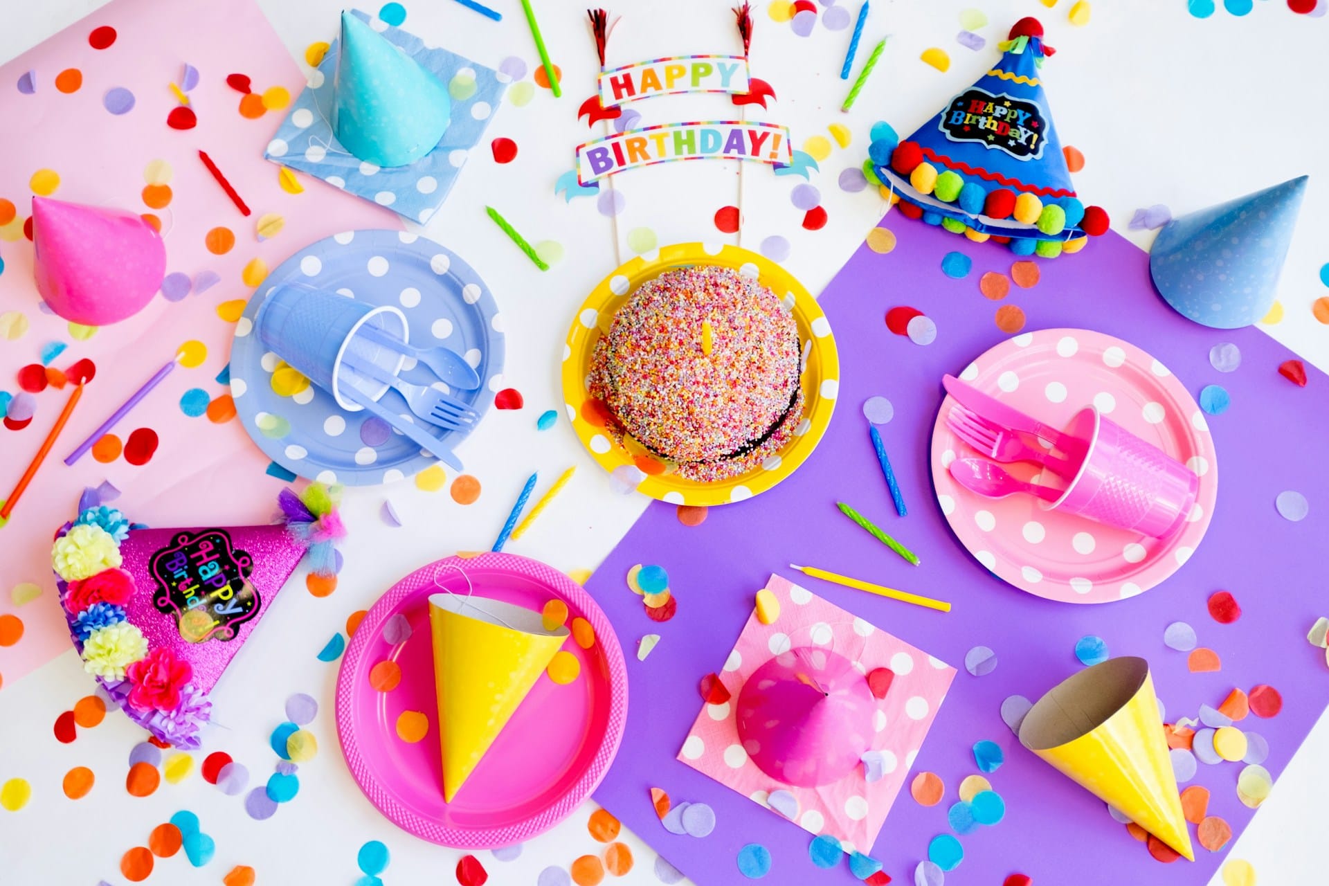 party table with an assortment of colourful napkins, paper plates, party hats, plastic cutlery with confetti sprinkled everywhere