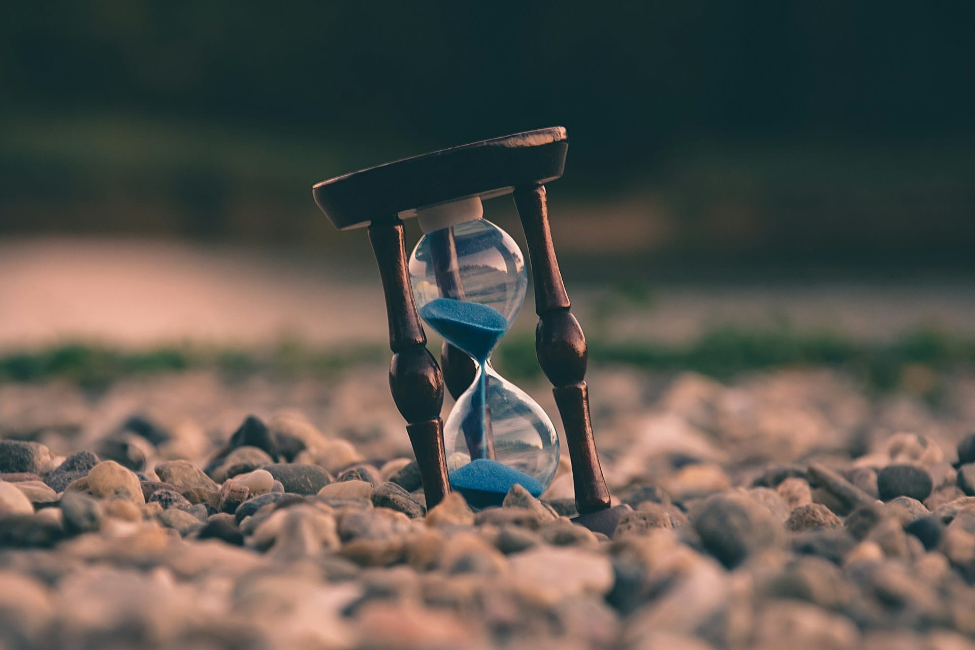a wooden hourglass with blue sand set on a bed of pebbles