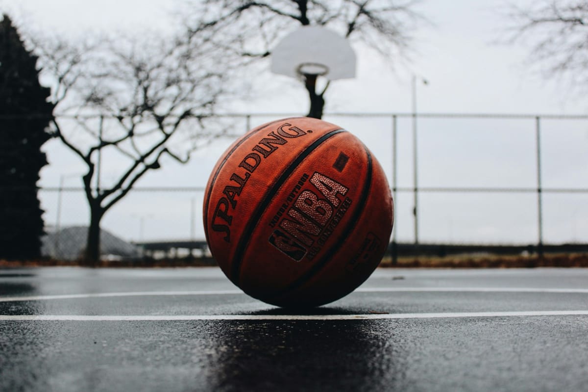 a Spalding basketball resting on a grey court with a blurred grey background featuring a hoop and a leafless tree