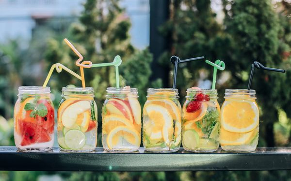 a row of six mason jars filled with fruit slices in water