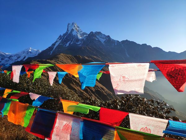 buntings of different colours hung on a clothesline against the backdrop of a snow-capped mountain peak