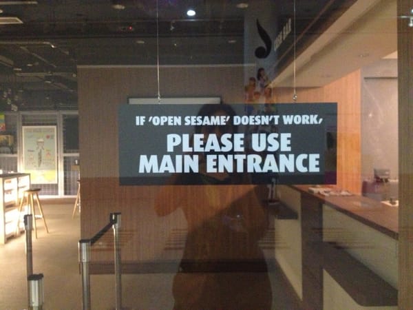 glass door to a cafe with a sign that says, "If open sesame doesn't work, please use main entrance."