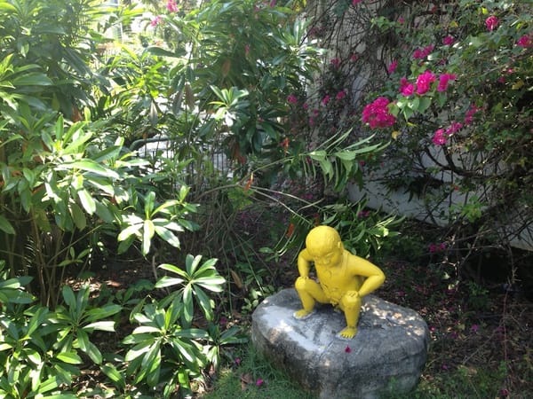 statue of a yellow boy squatting on a rock amid various plants