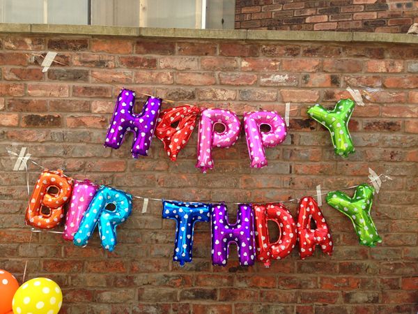 mylar balloons spelling Happy Birthday hung on a brick wall