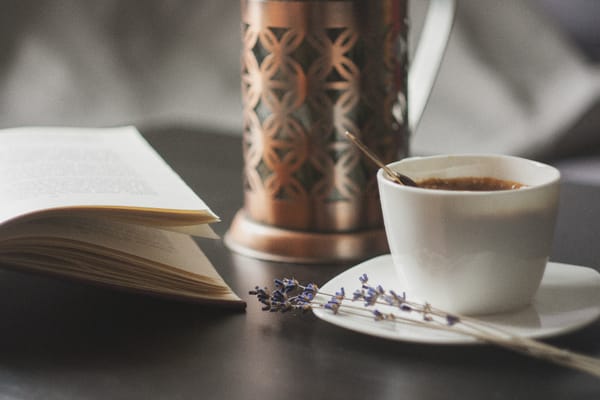 a book, a cup of coffee, a sprig of lavender and a lamp arranged aesthetically on a tabletop 