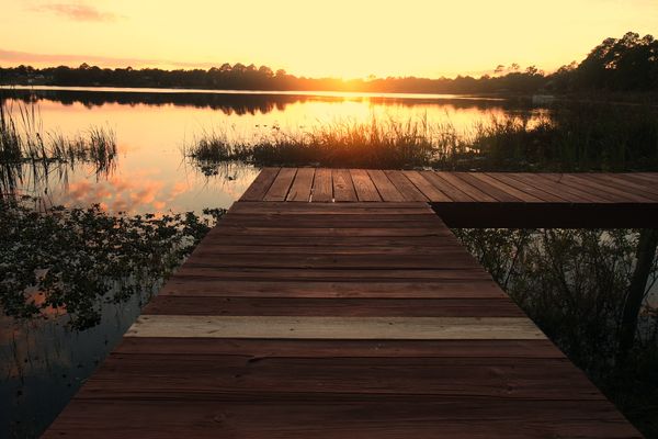 wooden deck facing a pond with the sun rising in the horizon beyond