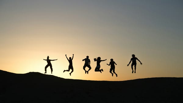 silhouettes of six people jumping against sunrise on the horizon
