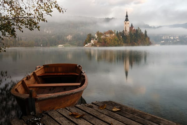 misty lakeside morning featuring a canoe by a deck and a castle on the far end of the lake