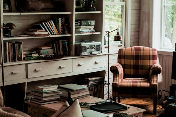 a cozy reading room with a shelf full of books and a wide upholstered chair