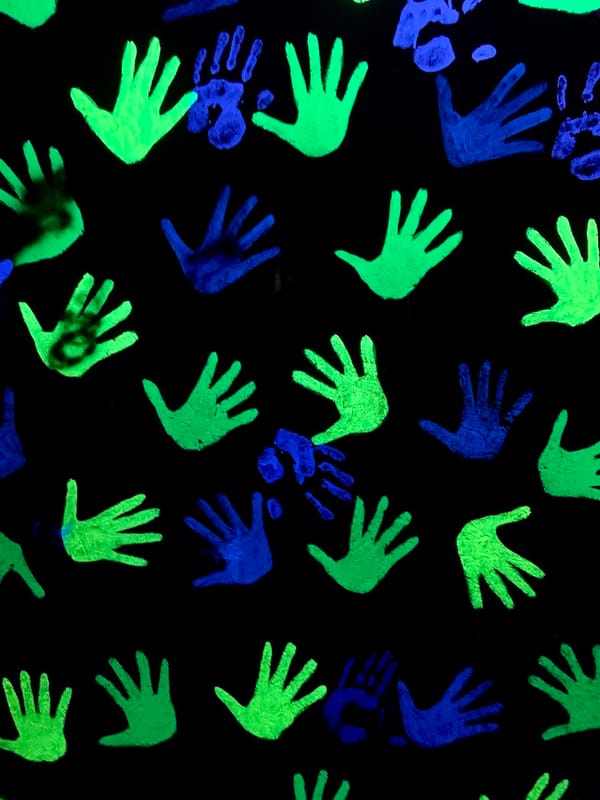 handprints in neon green and blue on a black wall