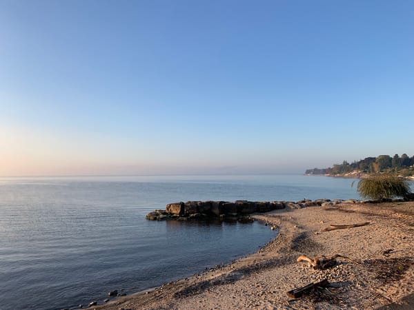 sandy shore by Lake Ontario under a blue sky and the dawn-pink of the horizon