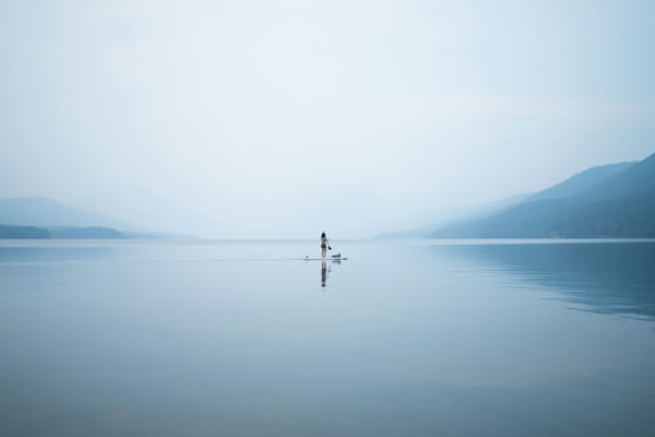 solo kayaker on a lake with pale blue silhouettes of mountains in the distance