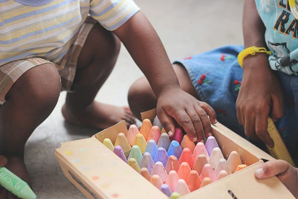 children reaching for a box of colourful chalks